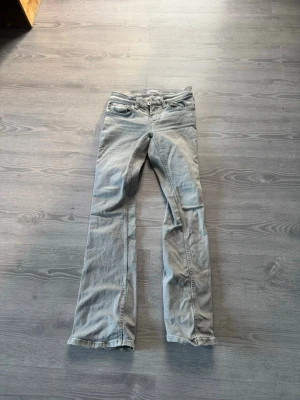 Ljusgrå bootcut jeans - Säljer ett par ljusgrå jeans med bootcut passform och klassisk femficksdesign. Jeansen har bälteshällor och dragkedjegylf. Materialet ser ut att vara bomullsdenim med en mjuk känsla. Perfekta för en avslappnad och trendig look.