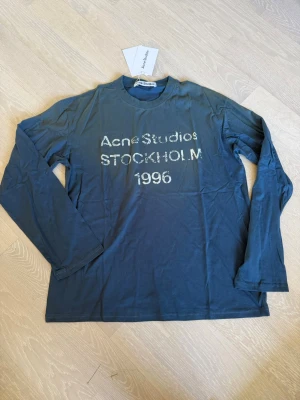 Blå långärmad topp Acne Studios M - Mörkblå långärmad topp från Acne Studios med tryck 'Acne Studios STOCKHOLM 1996' framtill. Tillverkad i mjuk bomull med normal passform och rund hals. Perfekt för en avslappnad och stilren look.