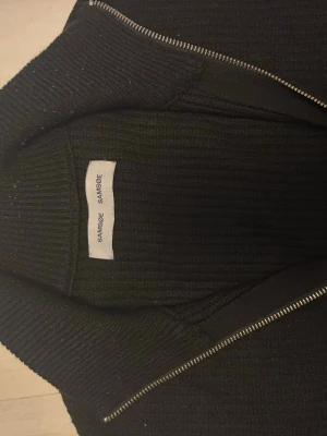 Svart ziptröja, Samsøe Samsøe - Tröjan är i grymt skick utom ett litet hål, Skick 9/10 , köpt i butik. Storleken sitter som lite mellan M och L. BILD PÅ HÅL FINNS PÅ SISTA BILDEN. Skriv vid övriga funderingar!:)