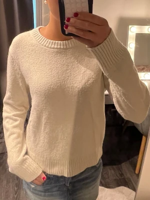 Krämvit stickad tröja - Mysig krämvit stickad tröja med rund halsringning och ribbade muddar vid ärmslut och nederkant. Tröjan har en enkel och stilren design som passar perfekt till jeans eller kjol. Materialet ser mjukt och bekvämt ut, perfekt för kyligare dagar.