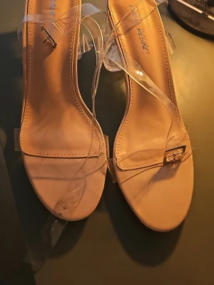 Beige pumps med transparenta remmar - Stilrena pumps i beige med transparenta plastremmar och fyrkantig tå. Klacken är medelhög och remmarna ger en modern look. Perfekta för dig som gillar minimalistisk och trendig stil.