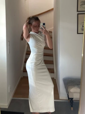 Vit långklänning med slits - En fin och elegant vit längre figurnära klänning från Zara. Endast använd vid ett studentfirande, så i fint skick förutom några fläckar som kan tvättas bort på begäran (se bilder). Den är i storlek M men passar mig som är storlek XS-S, är 163cm för referens. Passar bra som aftonklänning, på sommaren etc