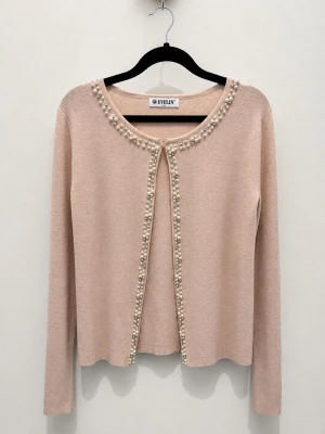 Beige rosa kofta med pärldetaljer - Supersöt beige rosa kofta från Evelyn med långa ärmar och rund halsringning. Koftan har dekorativa pärlor längs kanten och runt halsen som ger en elegant touch. Perfekt att slänga över en topp för en chic look. Den är aldrig använd eftersom att den tyvärr inte passar mig, säljs billigt nu pga flytt  :(