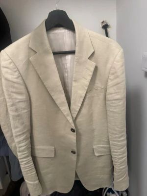 Beige linnékavaj tiger of sweden - Snygg beige kavaj i linne med två knappar framtill och klassiska fickor. Kavajen har smal passform, slits bak och är helfodrad. Perfekt för en stilren och avslappnad look.
