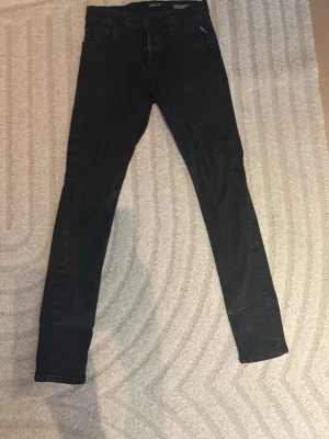 Svarta slim fit jeans från Replay - Säljer ett par svarta slim fit jeans från Replay, modell MickyM. Jeansen har klassisk femficksdesign, smal passform och är tillverkade i stretchigt denimtyg för extra komfort. Perfekta för en trendig och avslappnad look.