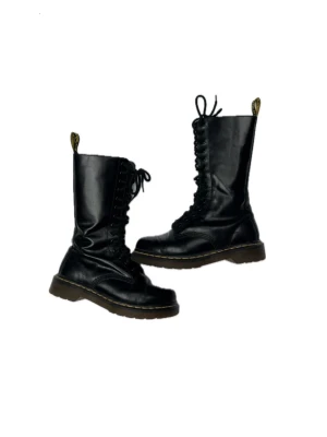 Svarta höga Dr Martens snörkängor i läder - Svarta höga Dr Martens snörkängor i äkta läder med grov sula och dragkedja på sidan. Klassisk modell med gul flärp bak och kontrastsömmar runt sulan. Storlek 37. Modell 1914. Nyskick och knappt använda.