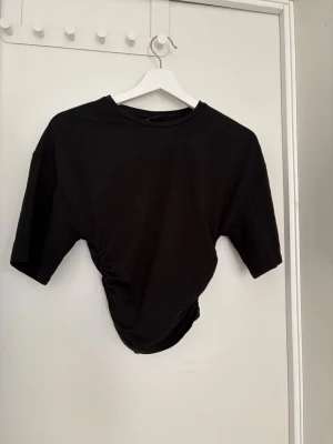 Svart tshirt med scrunch Gina - Säljer denna fina tshirt från Gina med scrunch i sidorna. Den är i storlek xs och i mycket bra skick!