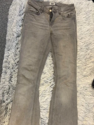 Gråa bootcut jeans från 157 - Snygga gråa bootcut jeans från 157 med klassisk femficksdesign och normalhög midja. Jeansen har dragkedjegylf och knapp, samt subtila slitningar för en avslappnad look. Perfekta till sneakers eller boots.