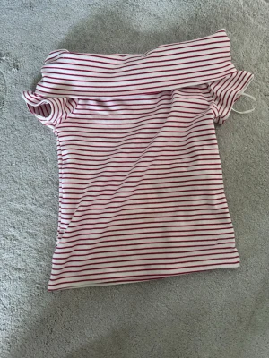 Randig offshoulder topp från Zara - Säljer en vit och röd randig offshoulder topp från Zara. Toppen har smala röda ränder och är axelbandslös med en tight passform. Perfekt för dig som gillar en enkel men trendig stil. Använd en gång