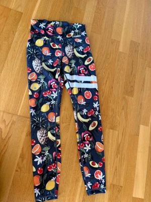 Mönstrade tights från Stronger - Färgglada tights från Stronger med fruktigt mönster i rött, gult, grönt och vitt. Tightsen har två vita ränder på ena benet. Perfekta för träning och riktigt snygga att matcha med en enkel topp.