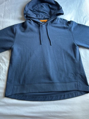 Blå hoodie med huva och dragsko - Snygg blå hoodie med huva och dragsko. Hoodien har långa ärmar, rundad nederkant och en stilren design utan tryck. Materialet ser ut att vara mjukt och bekvämt, perfekt för chill dagar. Passar dig som gillar enkel och clean stil.
