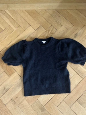 Marinblå stickad tröja med puffärm - Snygg marinblå stickad tröja med trendiga puffärmar och rund hals. Tröjan har ribbade muddar vid ärmslut och nederkant. Perfekt för dig som vill ha en enkel men ändå statement stickad topp.