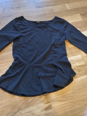 Mörkblå topp med volang från BikBok - Snygg mörkblå topp från BikBok med lång ärm och volang nedtill som ger en peplum-effekt. Tillverkad i mjuk bomull och har en enkel, rund halsringning. Perfekt för dig som vill ha en stilren men ändå trendig look. Även fast d står L så passar den mig bra som är XS och S