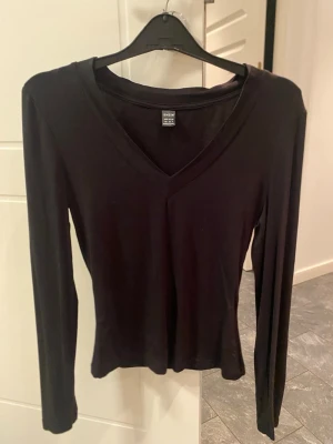 Basic svart långärmad tröja - En enkel och stilren svart långärmad topp med v-ringning. Perfekt att matcha med jeans eller kjol för en clean look. Tillverkad i mjukt material som känns skönt mot huden.
