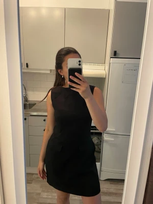 Svart ärmlös kortklänning NA-KD - Snygg svart kortklänning med figurnära passform och två dekorativa fickor framtill. Klänningen är ärmlös och har en klassisk, stilren design som passar perfekt till många olika tillfällen.
