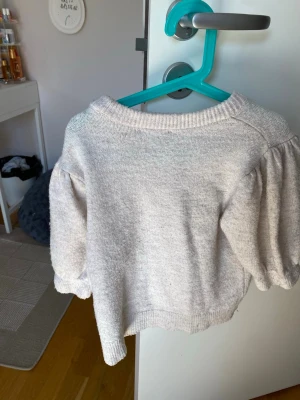 Ljusgrå stickad tröja med puffärm och ett litet hål men den är användbar  - Supersöt ljusgrå stickad tröja med puffiga ärmar och ribbade muddar. Tröjan har en rund halsringning och är gjord i mjukt material som känns skönt mot huden. Perfekt för dig som gillar en enkel men trendig look.