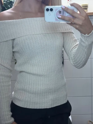Off shouldertröja offwhite - Trendig off shoulder stickad tröja i beige med ribbad struktur. Långa ärmar och bred krage som vilar över axlarna. Perfekt för hösten! Har en liten fläck framtill som dock inte syns under det med vikta❣️