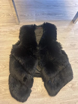 Svart fluffig pälsväst - Snygg svart pälsväst med mjuk och fluffig fuskpäls. Västen har en öppen front och är fodrad på insidan för extra komfort. Perfekt för att lyfta vilken outfit som helst med en trendig touch.