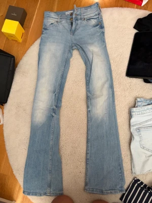 Ljusblå utsvängda jeans Bershka - Säljer ett par ljusblå jeans från Bershka i storlek 32. Jeansen har utsvängda ben och klassisk femficksdesign med dubbla knappar i midjan. Snyggt slitna detaljer framtill och tillverkade i denim. Perfekta för en trendig och avslappnad look.
