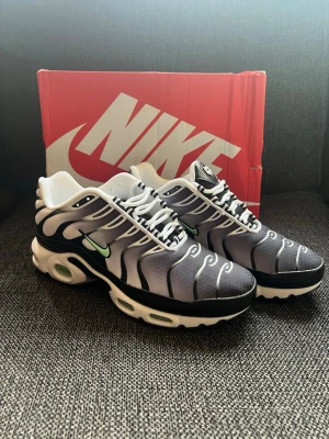 Nike Air Max Plus svart/vit - Nike Air Max Plus sneakers i svart och vitt med ikoniska vågmönster och mintgrön Swoosh. Skorna har en chunky sula med synliga Air-enheter och vita detaljer. Ovandelen är i mesh och syntet för en sportig vibe. Perfekta för dig som vill sticka ut med din sneakerstil.          Kartongen är skadad pga av transport. Priset kan diskuteras vid snabb affär.