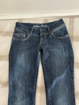 Mörkblå bootcut low wasted jeans Hilfiger Denim - Säljer dessa super snygga jeans, då de tyvärr är på tok för långa på mig som är 160 cm. Skulle tro att dom sitter längdmessigt bra på dig som är 170-175.  Dom har en tydlig bootcut, och en låg midja. Dom är gjord i 60% bomull, vilket gör att dom inte har så mycket stretch, men är istället väldigt hållbara! Detta är dessutom en gammal modell som inte säljs längre. Perfekt för dig som gillar 2000s jeans! Hör av er vid eventuella frågor                                             Storlek: W27 L34
