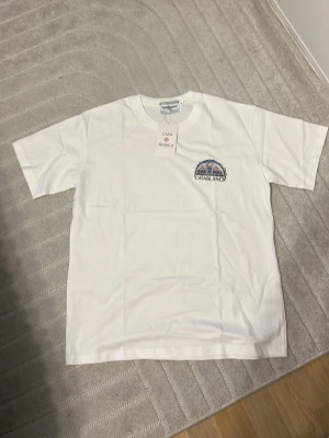 Vit t-shirt från Casablanca - Vit t-shirt från Casablanca med ett broderat motiv och logga på bröstet. Klassisk rund hals och korta ärmar. Tillverkad i mjuk bomull för en skön känsla. Perfekt för en clean och stilren look.