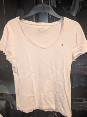 Ljusrosa t-shirt från Tommy Hilfiger - Snygg ljusrosa t-shirt från Tommy Hilfiger med liten broderad logga på bröstet. T-shirten har rund halsringning och är tillverkad i mjukt bomullsmaterial. Inga synliga fläckar eller defekter. Skapa en bundle för bättre pris