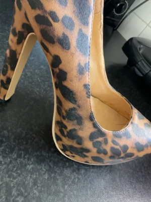 Leopardmönstrade pumps med hög klack - Säljer ett par snygga pumps med leopardmönster och hög klack. Skorna har rundad tå och är i ett konstlädermaterial med beige insida. Perfekta för dig som vill sticka ut och addera lite edge till din outfit.