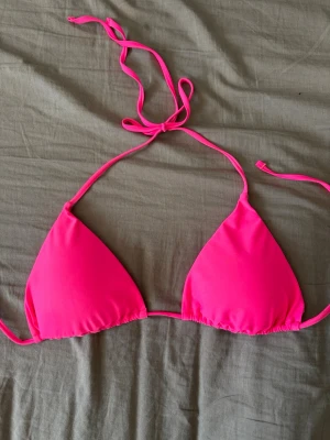 Rosa bikinitopp  - Säljer en snygg trekantsbikini i starkt rosa färg. Överdelen har tunna band som knyts i nacken och ryggen för justerbar passform. Perfekt för lata dagar på stranden eller poolen!