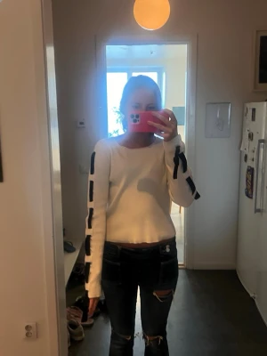 Vit stickad tröja med svarta detaljer - Vit ribbstickad tröja med svarta blockdetaljer längs ärmarna. Tröjan har rund halsringning och långa ärmar. Materialet ser ut att vara mjukt och stretchigt, perfekt för en avslappnad och trendig look.