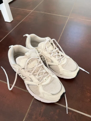 New Balance 408 - Snygga beige sneakers från New Balance med klassisk mesh och mocka på ovandelen. Skorna har vita snören, diskret logga på sidan och en chunky sula för extra komfort. Perfekta för dig som gillar stilrena och sportiga vibes.