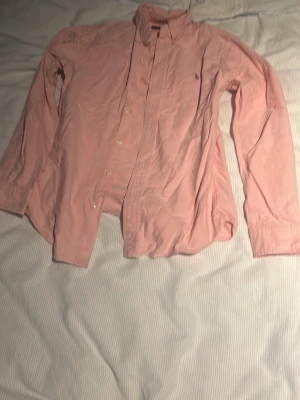 Rosa skjorta från Ralph Lauren S - Säljer en klassisk rosa skjorta från Ralph Lauren i slim fit-modell. Skjortan har långa ärmar, knappar framtill och en liten broderad logga på bröstet. Tillverkad i mjuk bomull, perfekt för en clean och stilren look.