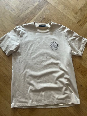 Beige Chrome Hearts t-shirt - Snygg beige t-shirt från Chrome Hearts med svart logga tryckt på bröstet och stort tryck på ryggen. 