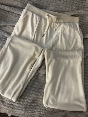 Vita juicy couture byxor🤍 - Säljer ett par riktigt sköna vita juicy couture mjukisbyxor med dragsko i midjan och broderad bokstavsdetalj på ena benet. Byxorna har fickor och är gjorda i ett mjukt, fleeceliknande material som känns lyxigt mot huden. Perfekta för chill dagar hemma eller när du vill vara bekväm.Original pris: 1200kr💞💞