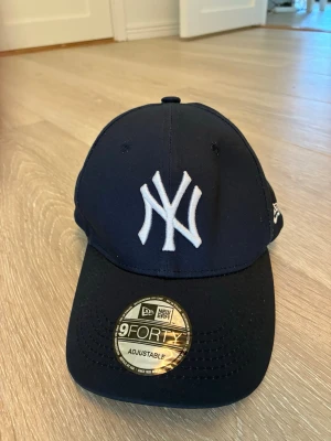Mörkblå New Era Yankees keps - Snygg mörkblå keps från New Era med klassisk New York Yankees-logga broderad i vitt framtill. Modellen är 9FORTY och har justerbar rem bak för perfekt passform. Kepsen är tillverkad i ett tåligt tyg och har böjd skärm.