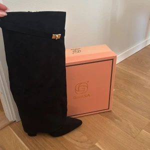 Svarta boots från Givana - Snygga svarta boots från Givana i mockaimitation med spetsig tå och bred klack. Dekorativt band med guldfärgat spänne upptill ger en trendig touch. Dragkedja på insidan för enkel på- och avtagning. Perfekta för att lyfta din outfit. Använda 1 gång,  nypris 1500 säljer då de inte passade!