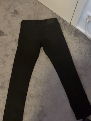 Jack and Jones  - Säljer ett par svarta skinny jeans med klassisk femficksdesign och hög midja. Jeansen har en stilren look och passar perfekt till en trendig vardagsoutfit. Materialet känns mjukt och stretchigt för extra komfort.