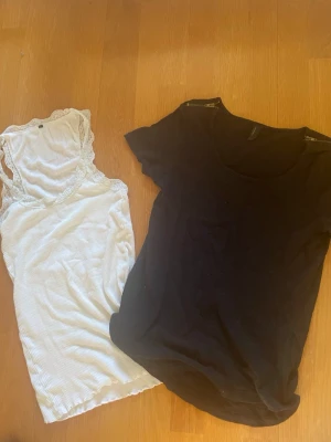 Vera Moda Svart t-shirt & vit spetslinnetopp - Två toppar: en svart enkel t-shirt med rund hals och kort ärm samt en vit ribbad linnetopp med spetsdetaljer vid axlarna. Perfekta basplagg att matcha till olika outfits.