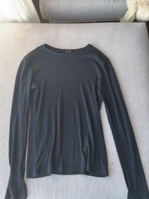 Svart ribbad långärmad topp - En svart långärmad topp med ribbad struktur och rund hals. Enkel och stilren modell som passar perfekt till jeans eller kjol. Tunn och smidig, lätt att matcha med andra plagg.