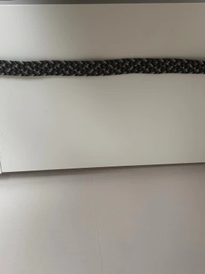 Flätat bälte från Onewear Sweden - Snyggt flätat bälte från Onewear Sweden i svart, grått och vitt. Bältet har en cool mönstrad look och detaljer i skinn. Perfekt för att lyfta vilken outfit som helst.