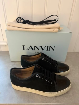Svarta Lanvin Cap Toe - Snygga svarta sneakers från Lanvin med ovandel i mocka och lackad tå. Skorna är storlek Uk 6 och är i ett mycket bra skick . Box, 2 dustbags, kvitto från care of carl och ett par helt nya skosnören medföljer! Pris 2199kr. Hör av dig vid funderingar! 📩