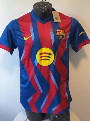 Barcelona matchtröja Nike blå/röd - Säljer en Barcelona matchtröja från Nike i blått och rött med gula detaljer och klubbmärke på bröstet. Tröjan har korta ärmar, randigt mönster och är tillverkad i polyester. Perfekt för fotbollsträning eller att bära som supporter.