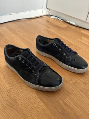 Mörkblå Lanvin Captoe - Säljer ett par mörkblå Lanvin Captoe. Skorna har svarta snören, metallfärgade öljetter och vit sula. Snygg kontrast mellan material och passar perfekt till streetwear eller casual stil.