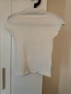 Vit ribbad polotopp från Zara - Säljer en vit ribbad polotopp från Zara i storlek S. Toppen har korta ärmar och en hög krage som ger en clean och stilren look. Perfekt att matcha med jeans eller kjol för en enkel men snygg outfit.