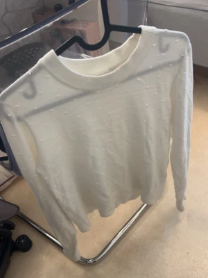 Vit stickad tröja från Kappahl - Säljer en vit stickad tröja från Kappahl i storlek S. Tröjan har diskreta små bollar i strukturen, rund halsringning och långa ärmar. Perfekt för dig som gillar en enkel men ändå detaljrik look.