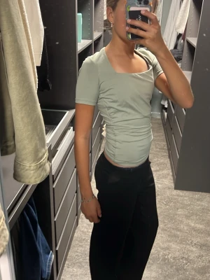 Ljusgrön croppad topp med rynk - Snygg ljusgrön croppad topp med korta ärmar och fyrkantig ringning. Toppen har rynkade sidor som ger en cool och smickrande passform. Perfekt till jeans eller kjol för en trendig look.
