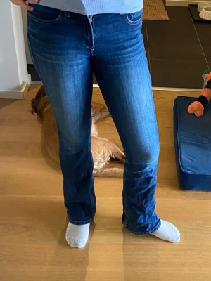 Mörkblå bootcut jeans ifrån Ariat jeans - Storlek 27 R. Nypris 1200kr. Säljer ett par mörkblå bootcut jeans med klassisk femficksdesign och dragkedja fram. Jeansen har en lätt tvättad look med subtila slitningar och är tillverkade i ett stretchigt denimtyg som sitter bekvämt. Perfekta för dig som gillar en tidlös och avslappnad stil.