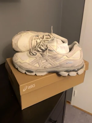 Vit/Biege Asics sneakers med mesh och mocka - Säljer ett par vita Asics sneakers med klassisk siluett. Skorna har ovandel i mesh och mocka, med Asics-logga på sidan. Sulan är chunky och ger en sportig vibe. Perfekta för dig som gillar stilrena och bekväma sneakers.