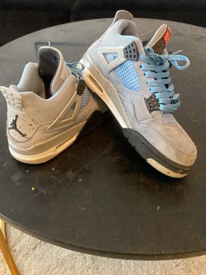 Jordan 4 University Blue sneakers - Säljer ett par Jordan 4 University Blue sneakers i ljusblå mocka med svarta och vita detaljer. Skorna har blå mesh på sidan, svarta plastdetaljer och ljusblå skosnören. Ikonisk Jumpman-logga på hälen och nummer 23 på plösen.