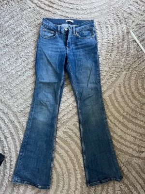 Blå bootcut jeans med medel hög midja  - Säljer ett par klassiska blå bootcut jeans med medel hög midja och fem fickor. Jeansen har en snygg tvätt och utsvängda ben, perfekta för en trendig och avslappnad stil. Tillverkade i denim med knapp- och dragkedjestängning framtill. Aldrig använda 💕